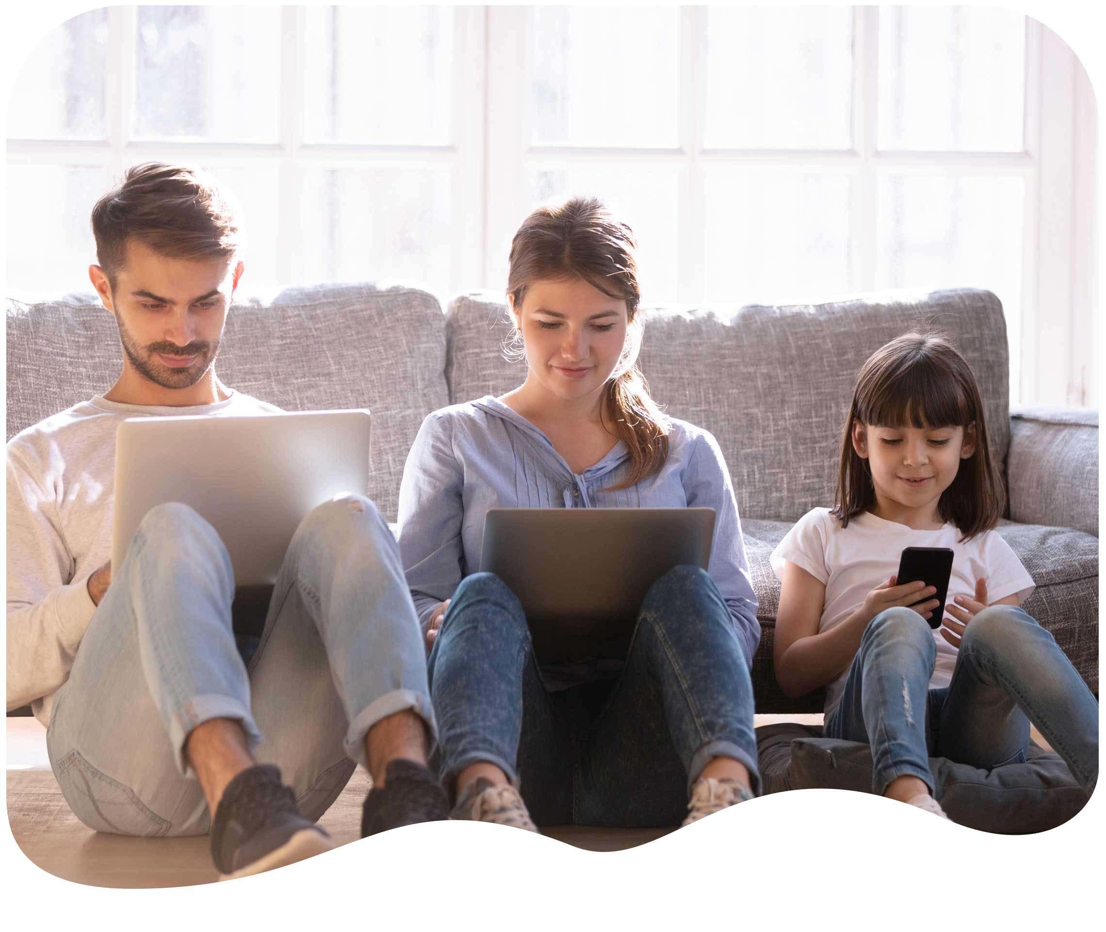 Dreiköpfige Familie sitzt auf dem Sofa und jeder schaut auf seinen eigenen Laptop oder das Smartphone