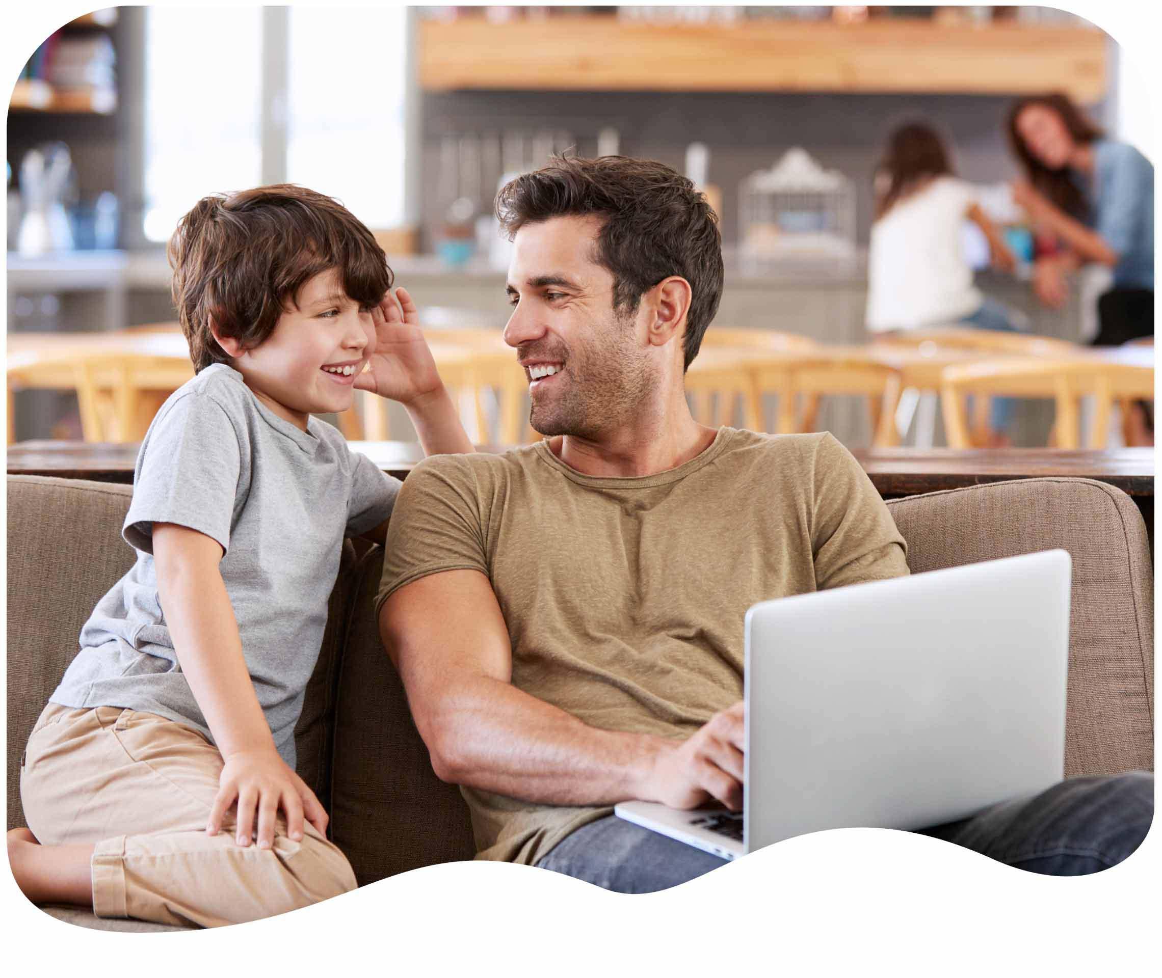 Vater lacht mit seinem Sohn vor einem Laptop