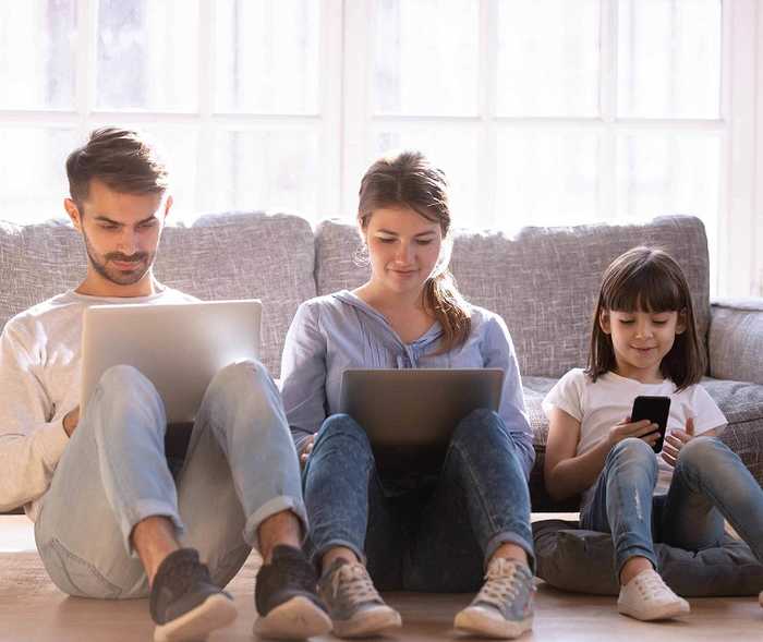 Familie sitzt auf dem Sofa und jeder schaut auf seinen eigenen Laptop oder Smartphone Familie sitzt auf dem Sofa und jeder schaut auf seinen eigenen Laptop oder Smartphone